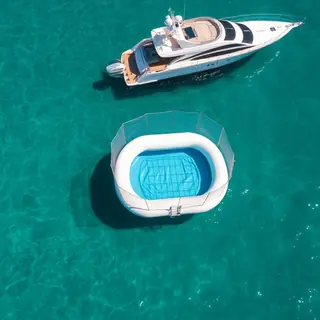 Piscina flutuante inflável ao lado de uma lancha em mar turquesa