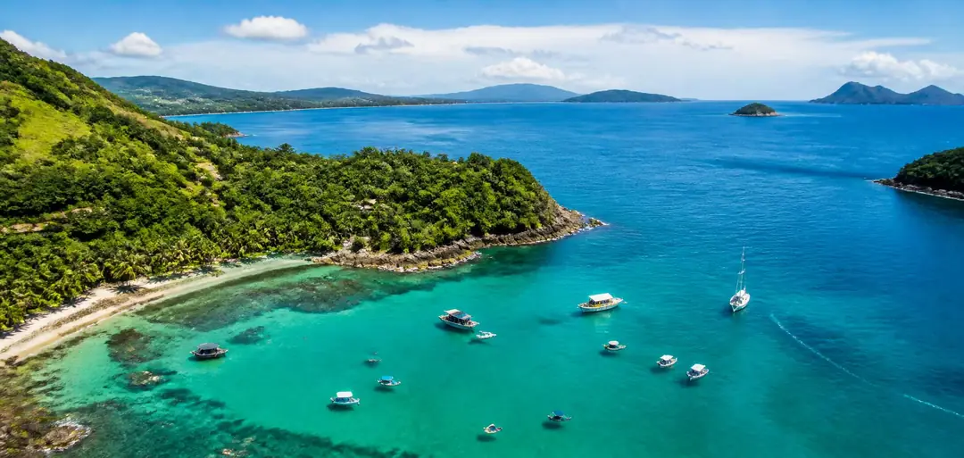 Vista aérea panorâmica do litoral com mar azul-turquesa e lanchas ancoradas